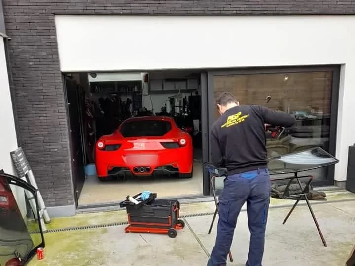 Rode Ferrari voor de garagepoort, met een monteur ernaast