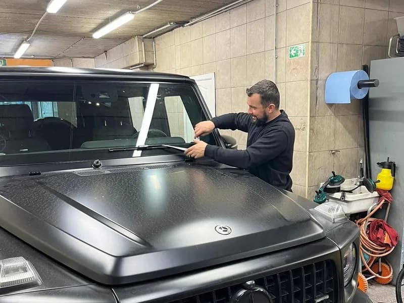 Monteur aan de voorruit van een matzwarte Mercedes G-klasse