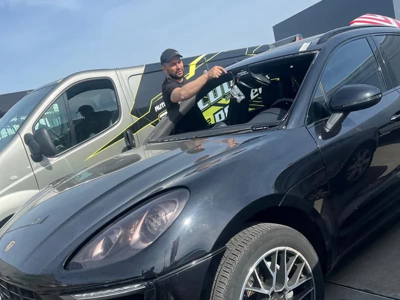 Monteur aan de ruitopening van een zwarte Porsche