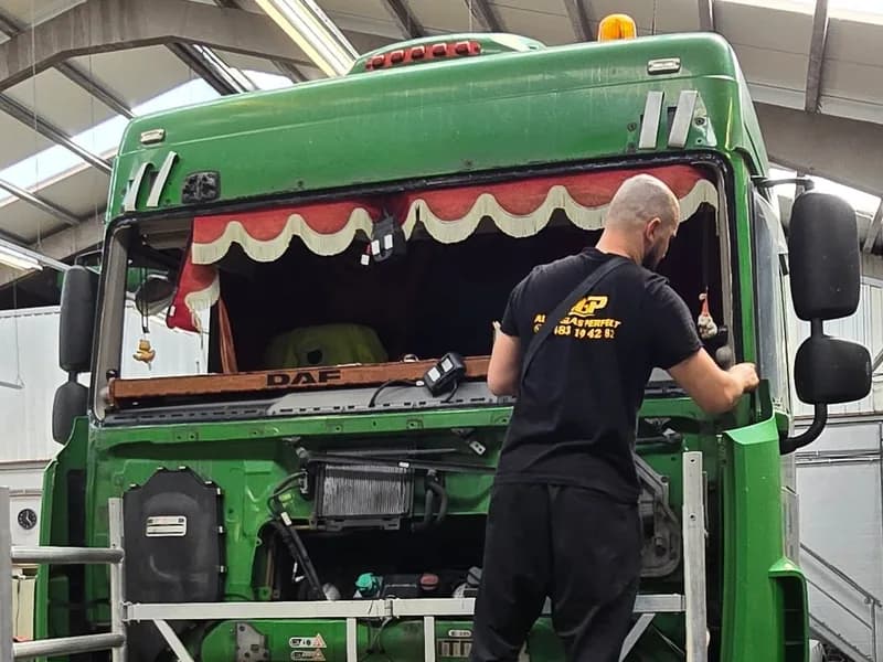 Monteur vervangt de voorruit van een groene truck vanaf de werkbrug