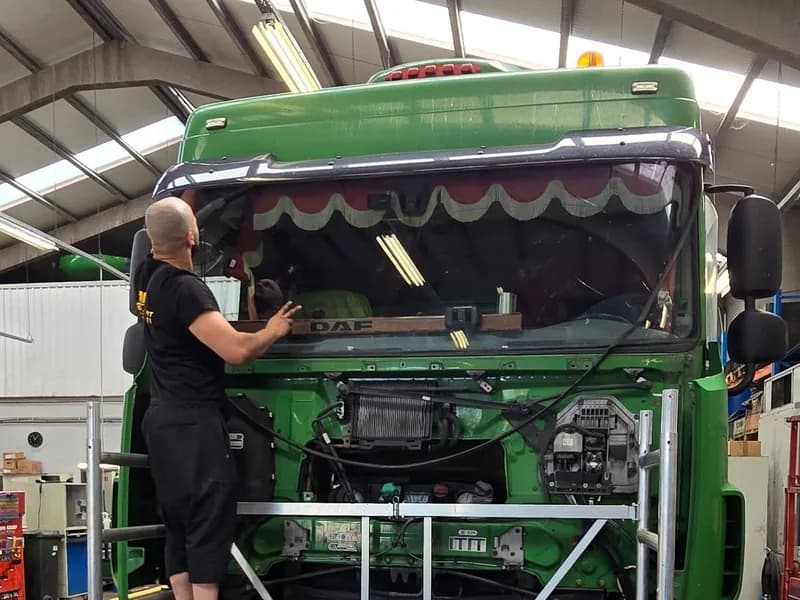Groene truck van opzij, met de monteur aan de ruitopening